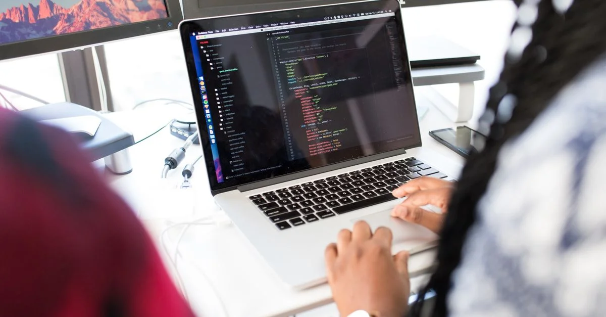 Une femme en train de coder sur un ordinateur portable dans un environnement de bureau moderne avec plusieurs écrans.