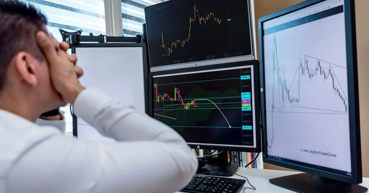 Homme frustré surveillant plusieurs graphiques de trading sur des écrans d'ordinateur dans un bureau.