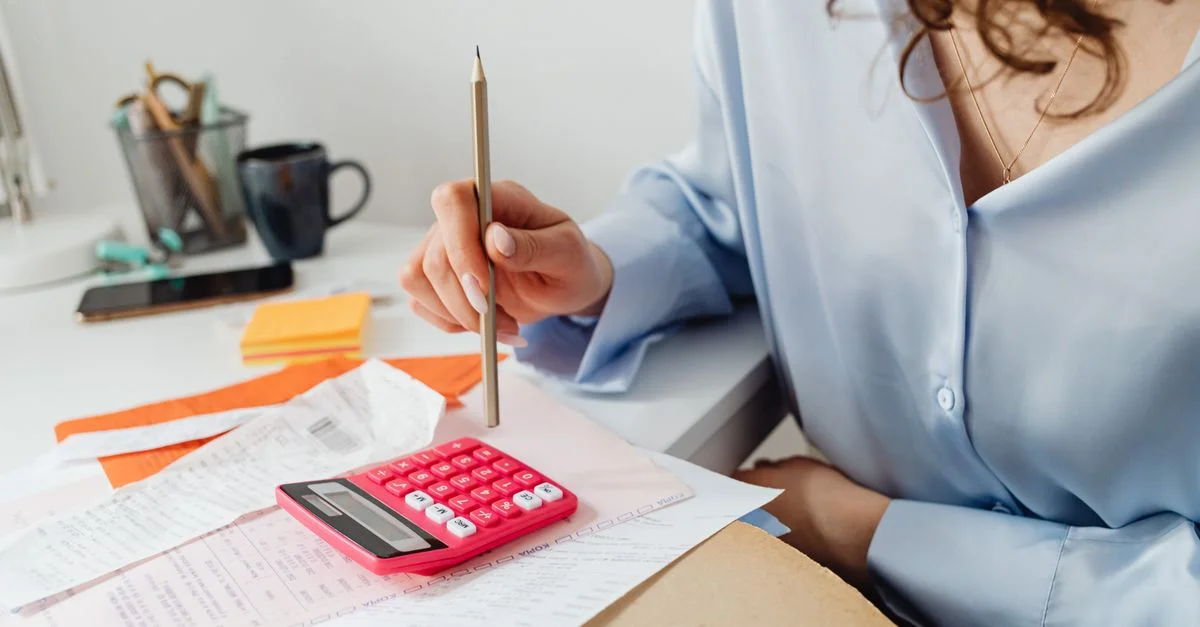 Une femme calcule des dépenses en utilisant une calculatrice et des papiers à son bureau.