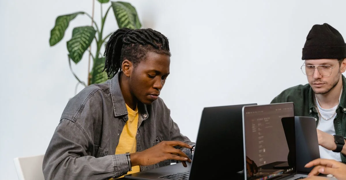Deux jeunes adultes travaillant ensemble sur des ordinateurs portables dans un bureau, se concentrant sur leurs tâches.
