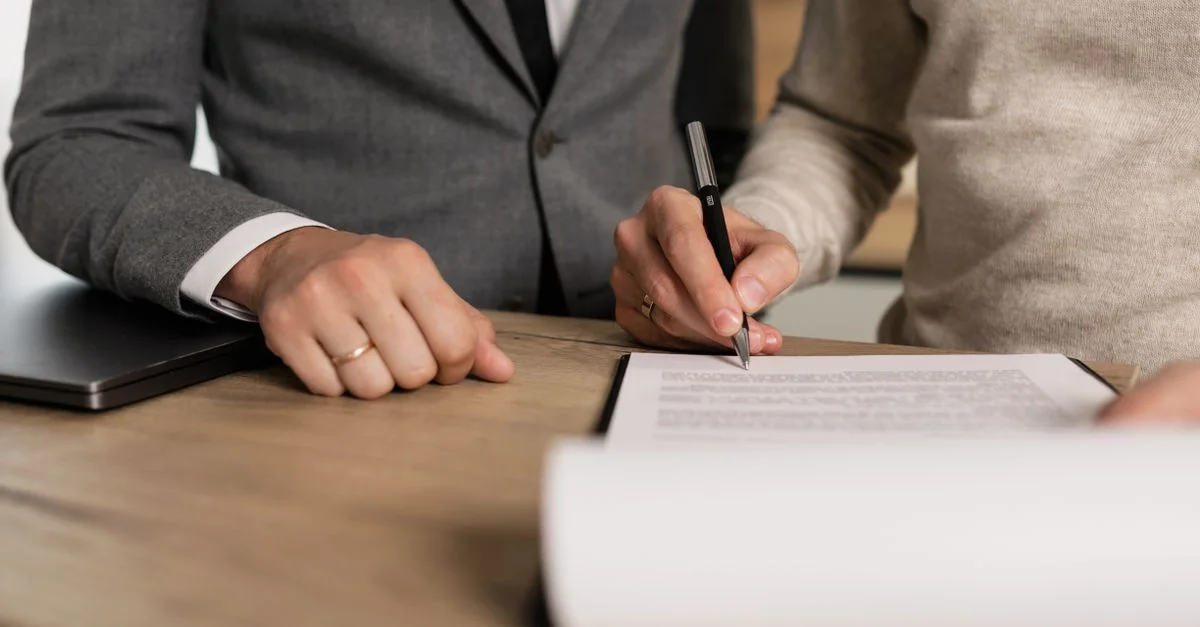 Gros plan sur des hommes d'affaires signant des documents sur une table en bois dans un bureau.