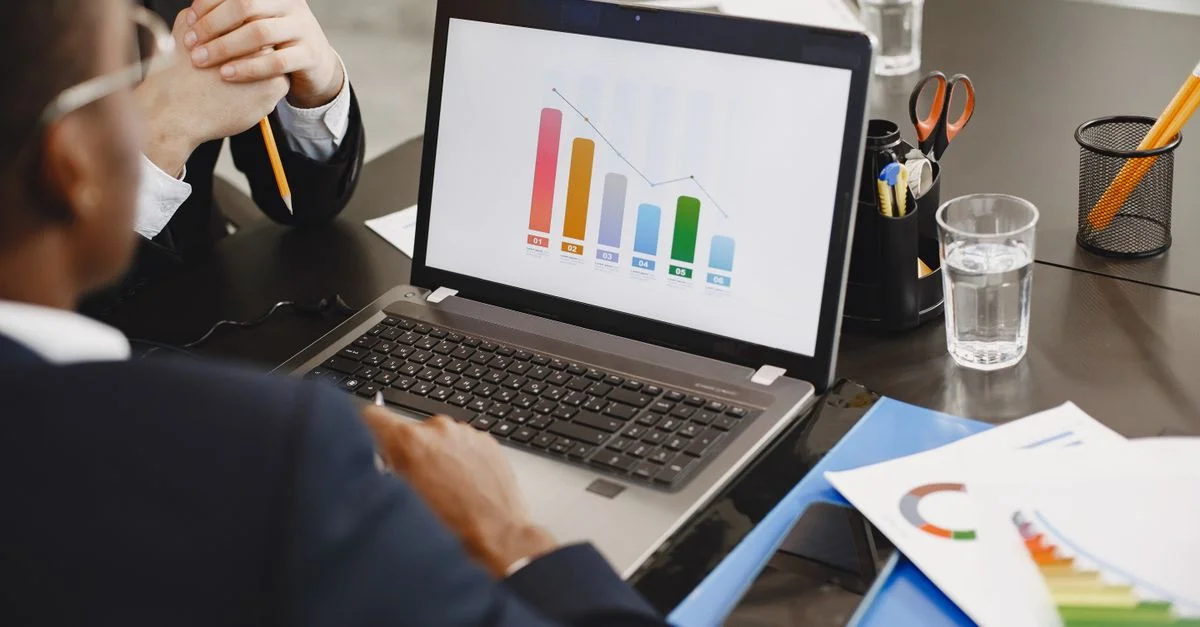 Deux professionnels analysant un graphique commercial sur un ordinateur portable lors d'une réunion.